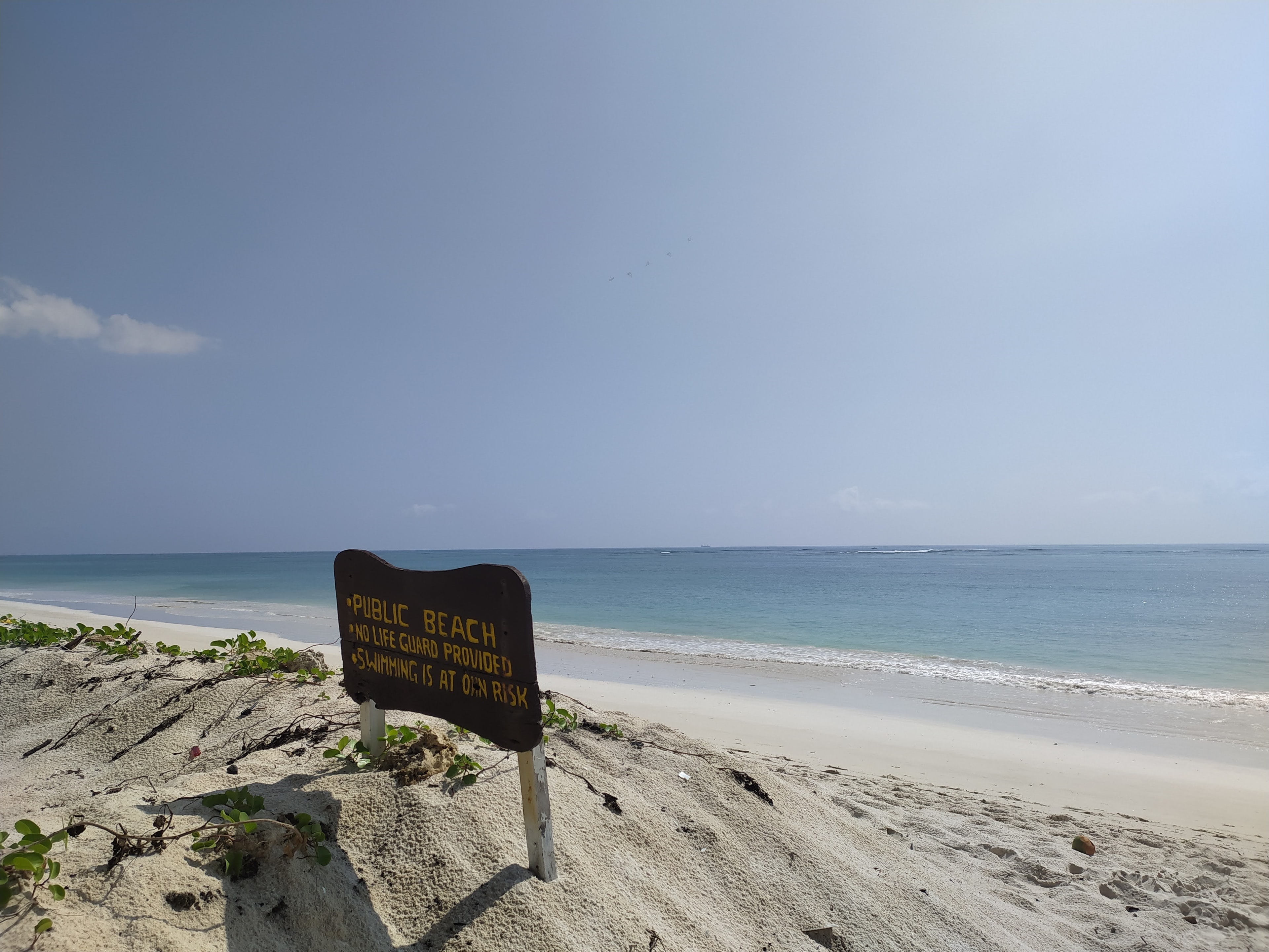 A weathered Public Beach sign on the dunes at Diani